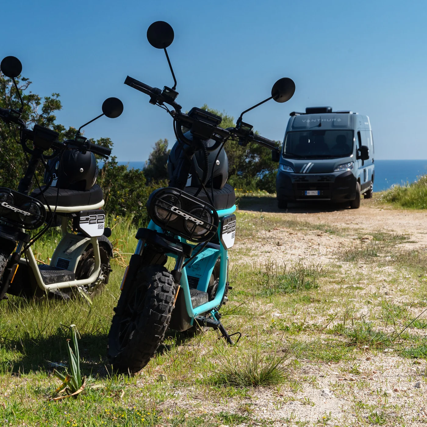 Drei elektrische Motorräder auf einem Weg mit einem Transporter im Hintergrund