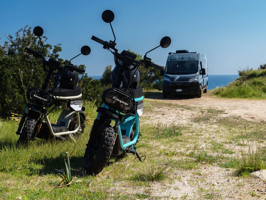 Drei elektrische Motorräder auf einem Weg mit einem Transporter im Hintergrund