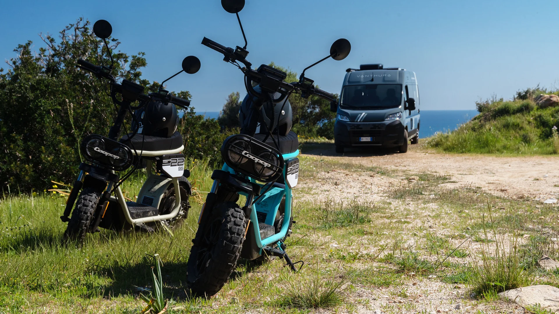Drei elektrische Motorräder auf einem Weg mit einem Transporter im Hintergrund