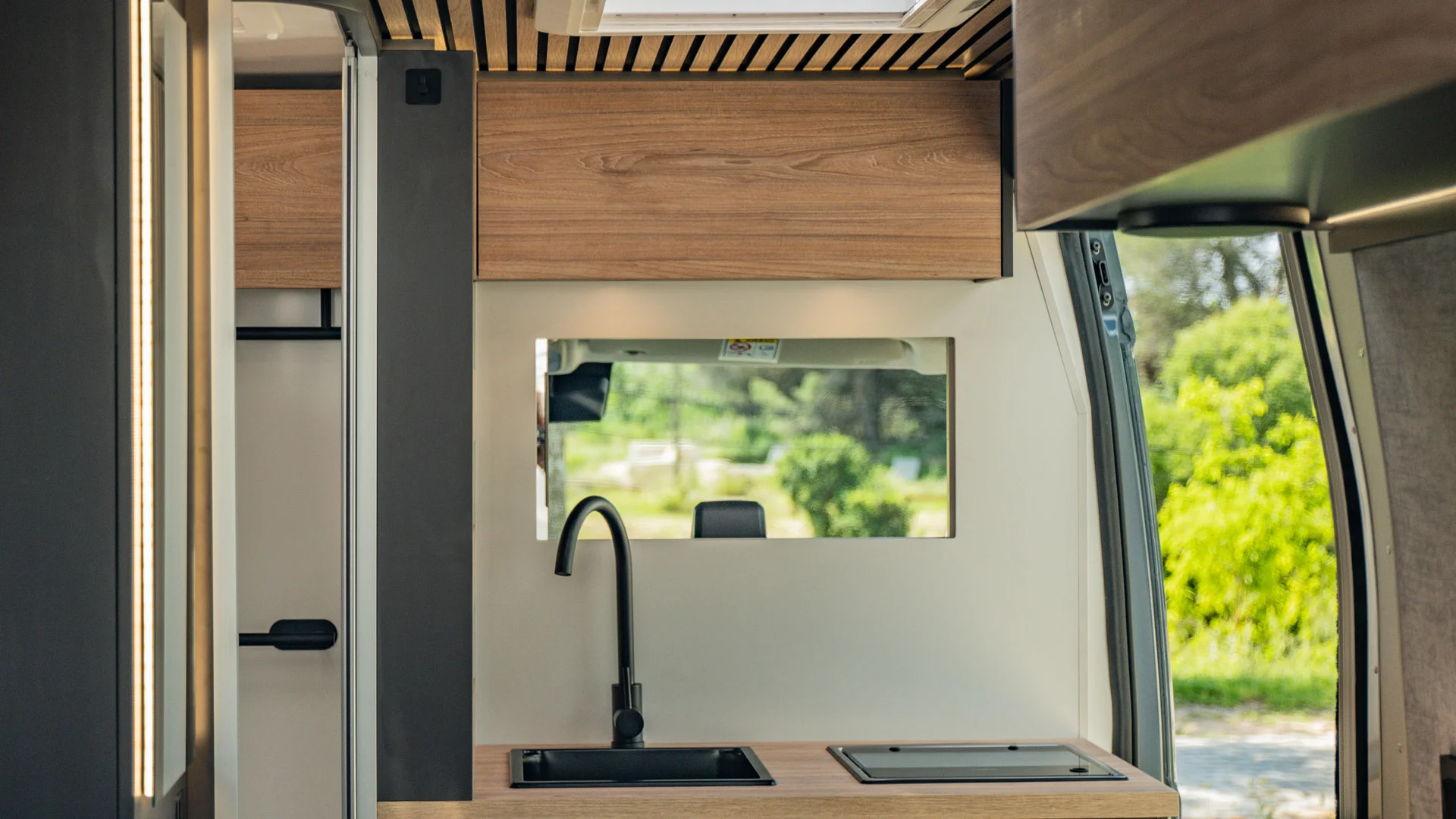Interno di un camper con cucina moderna e vista verde dalla finestra