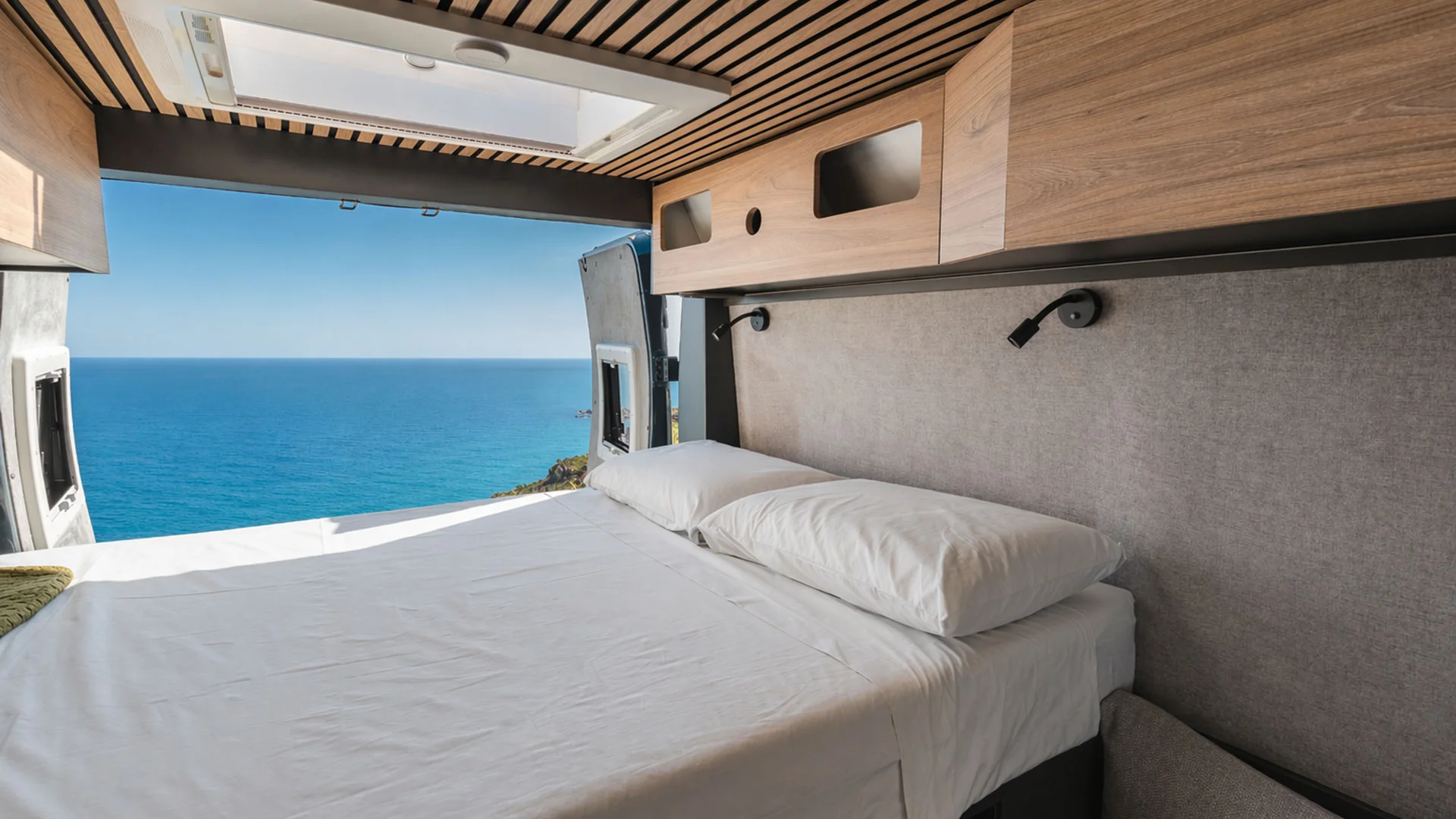 Bett im Wohnmobil mit Meerblick und hellen Holzeinbauten