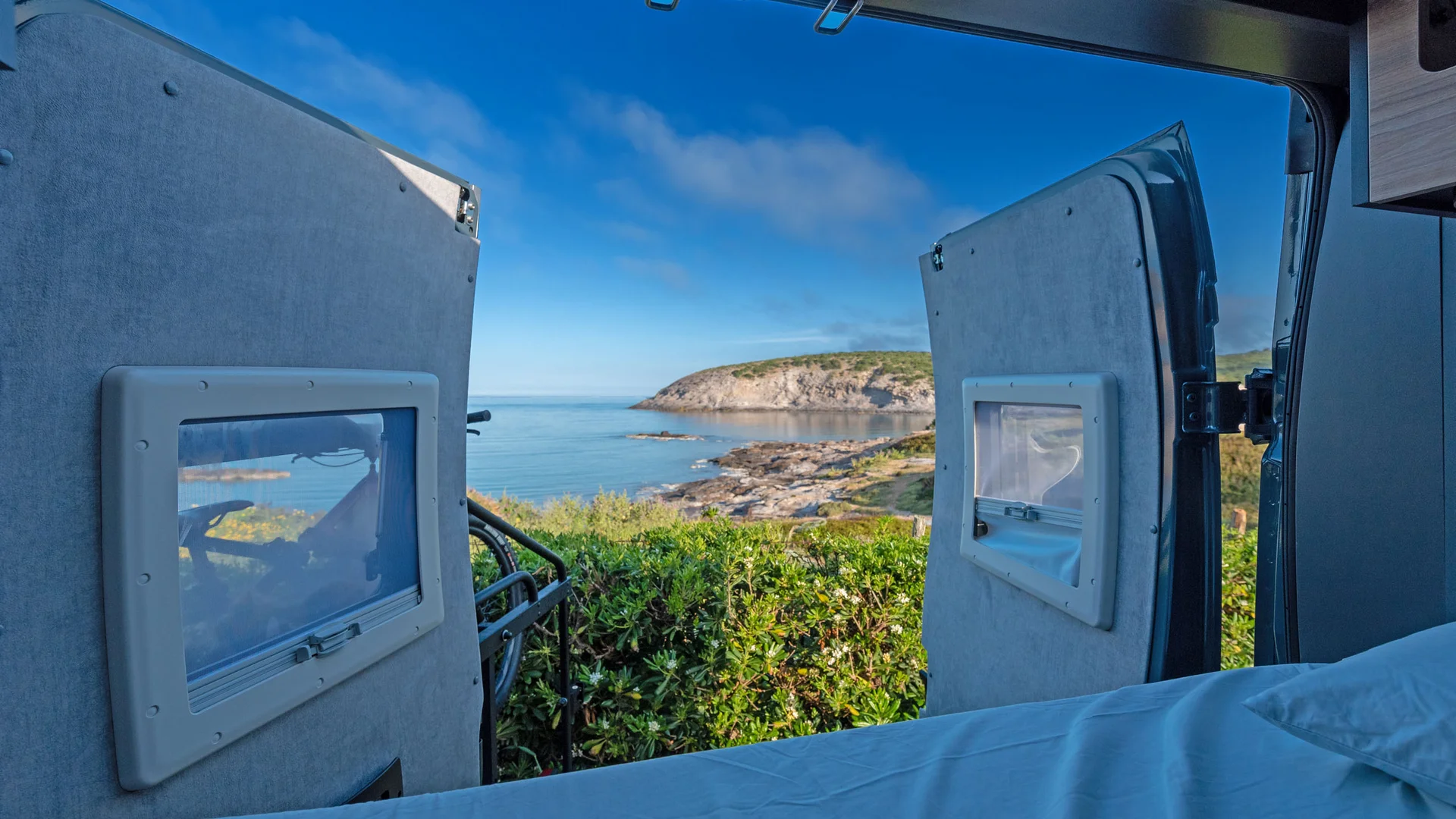 Blick vom Campingbett aufs Meer und eine Felsenküste unter blauem Himmel