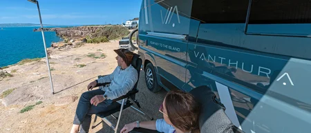 Due persone sedute vicino a un camper blu con vista sul mare