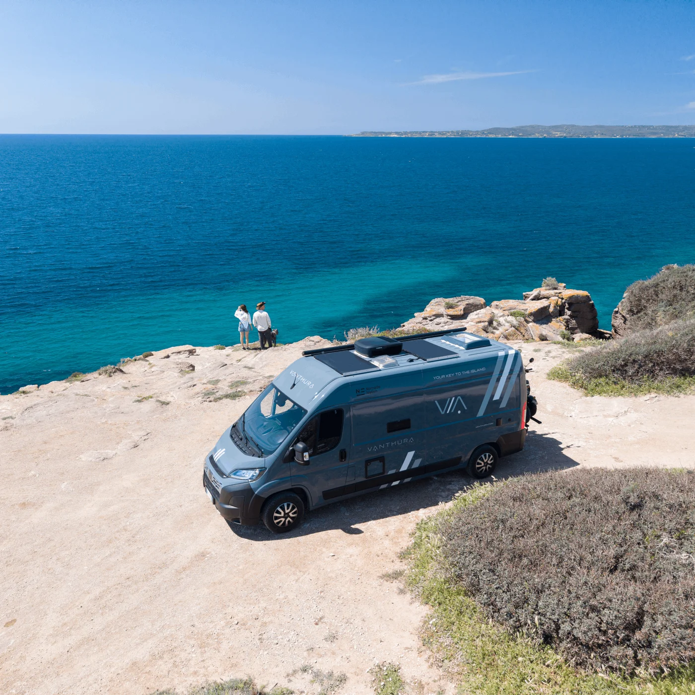 Van auf Klippe mit Meerblick und zwei Personen stehend