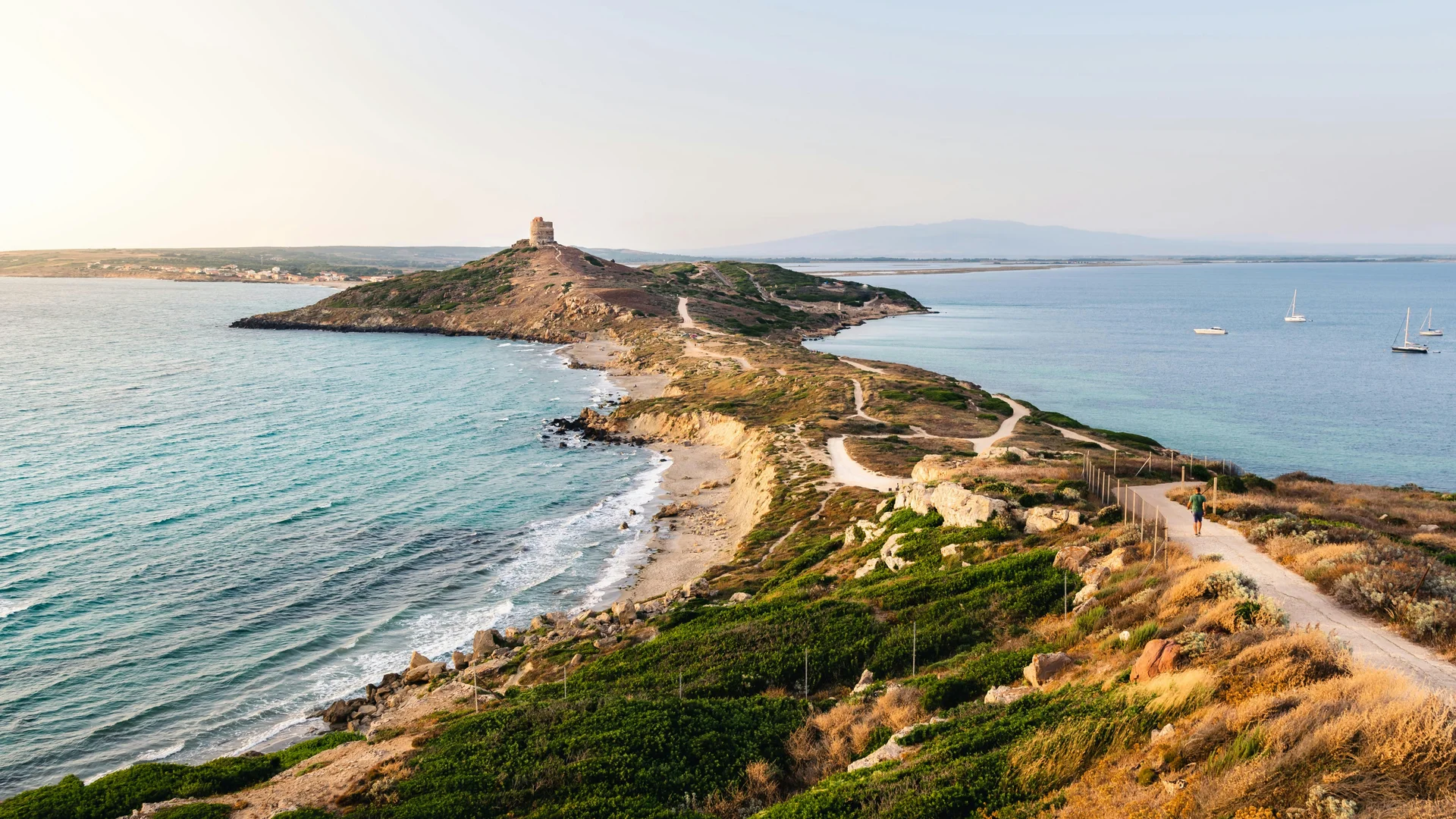 Sentiero costiero che porta a una torre su una penisola rocciosa con mare azzurro