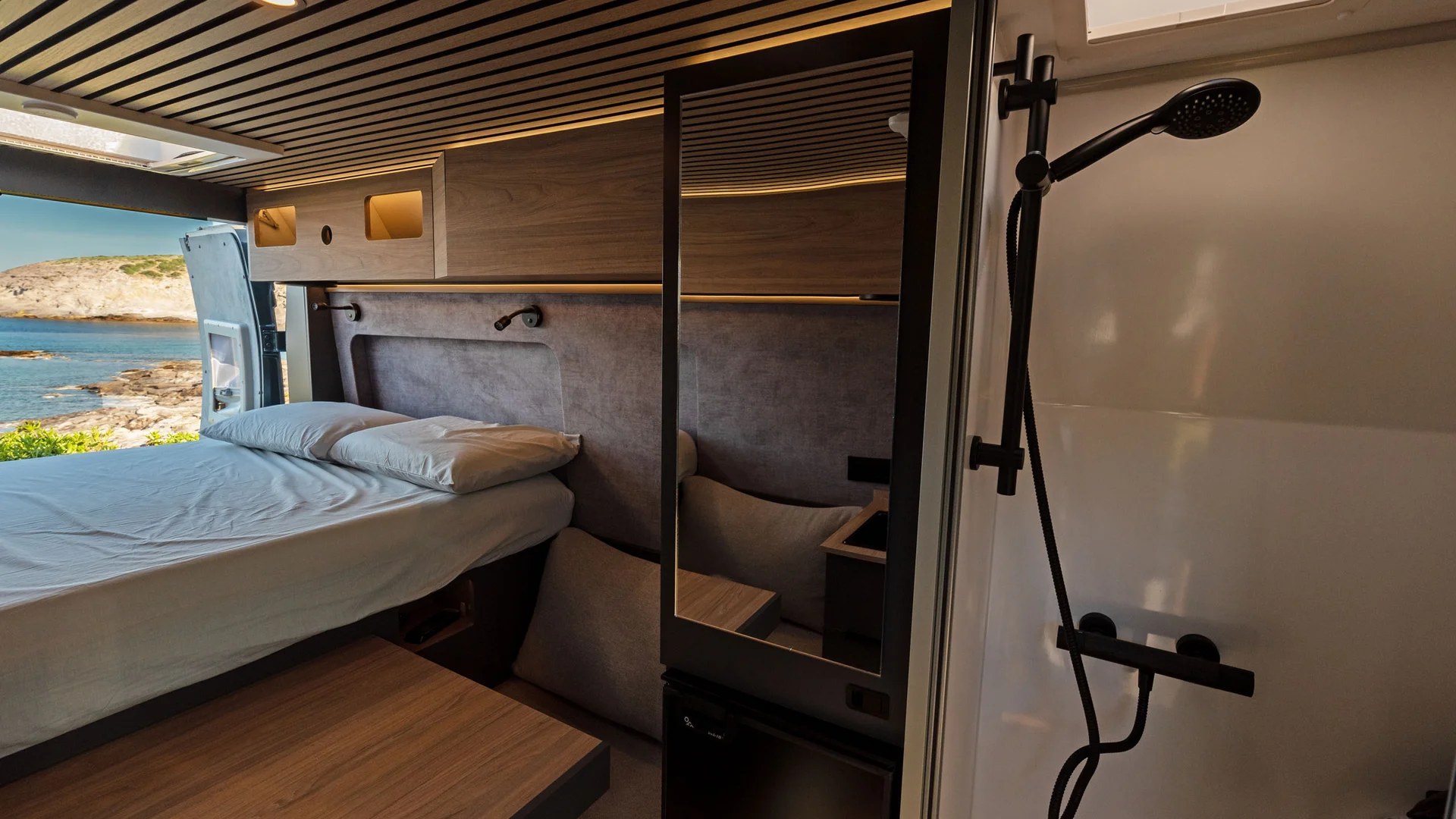 Innenraum eines Campers mit Bett, Tisch und moderner Dusche mit Meerblick