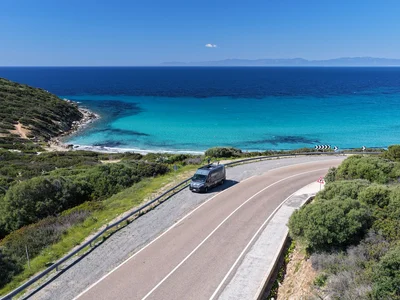 Küstenstraße mit Van am türkisfarbenen Meer und klarem Himmel