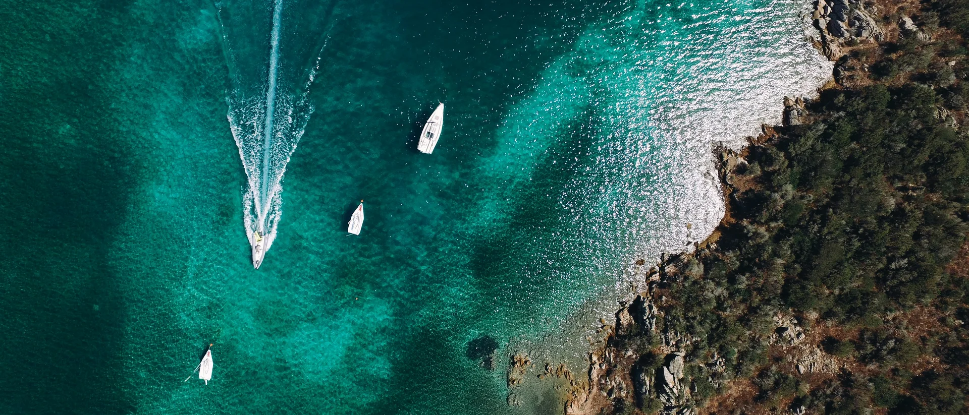 Barche nel mare turchese vicino alla costa rocciosa con vegetazione