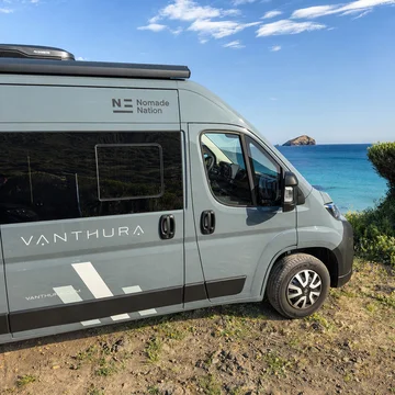Furgone da campeggio Vanthura vicino al mare con cielo azzurro e isola in lontananza