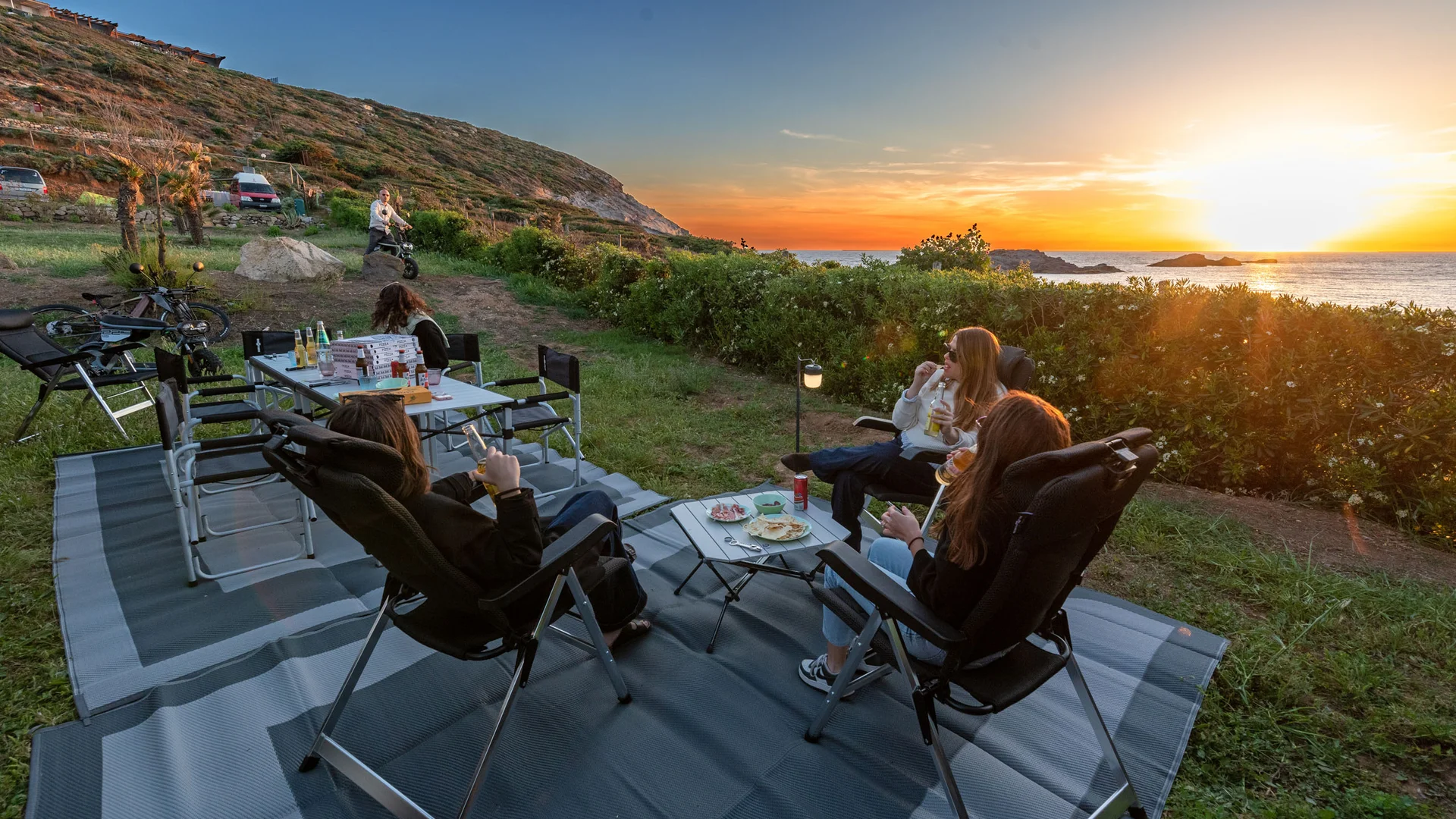 Personen entspannen auf Campingstühlen bei Sonnenuntergang am Meer