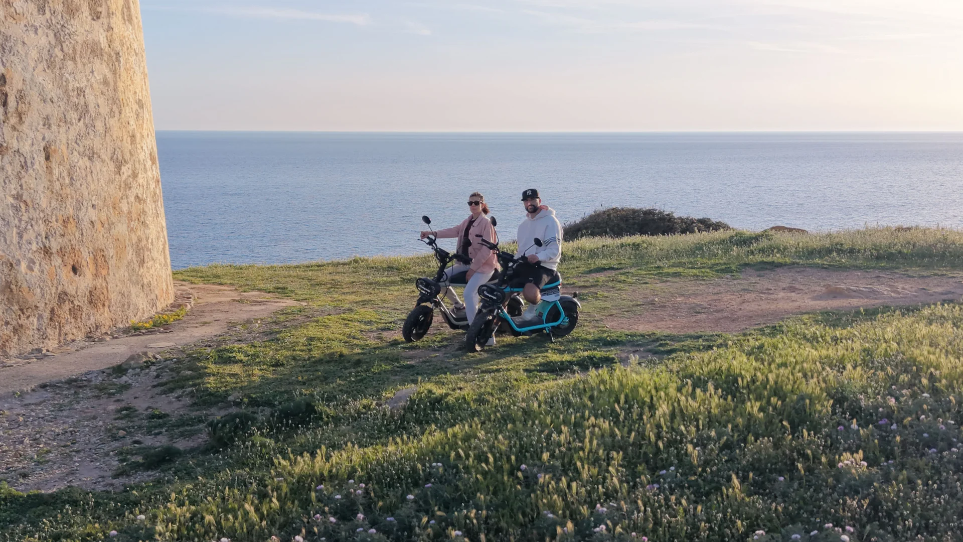 Paar auf Elektrofahrrädern am Meer neben einem Steinturm