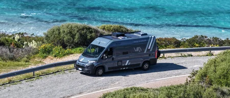 Wohnmobil auf einer Straße nahe türkisfarbenem Meer und grüner Vegetation