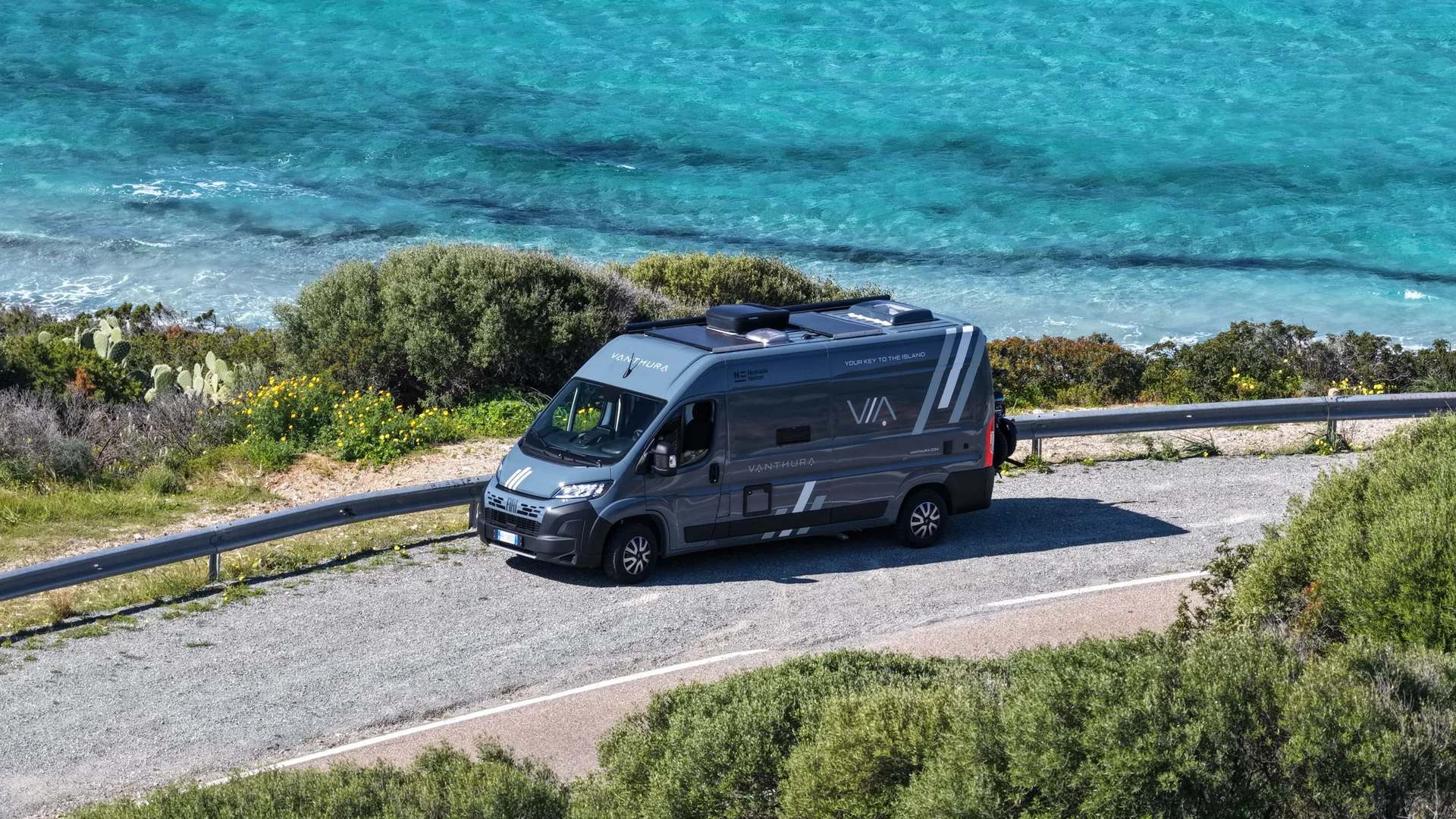 Wohnmobil auf einer Straße nahe türkisfarbenem Meer und grüner Vegetation