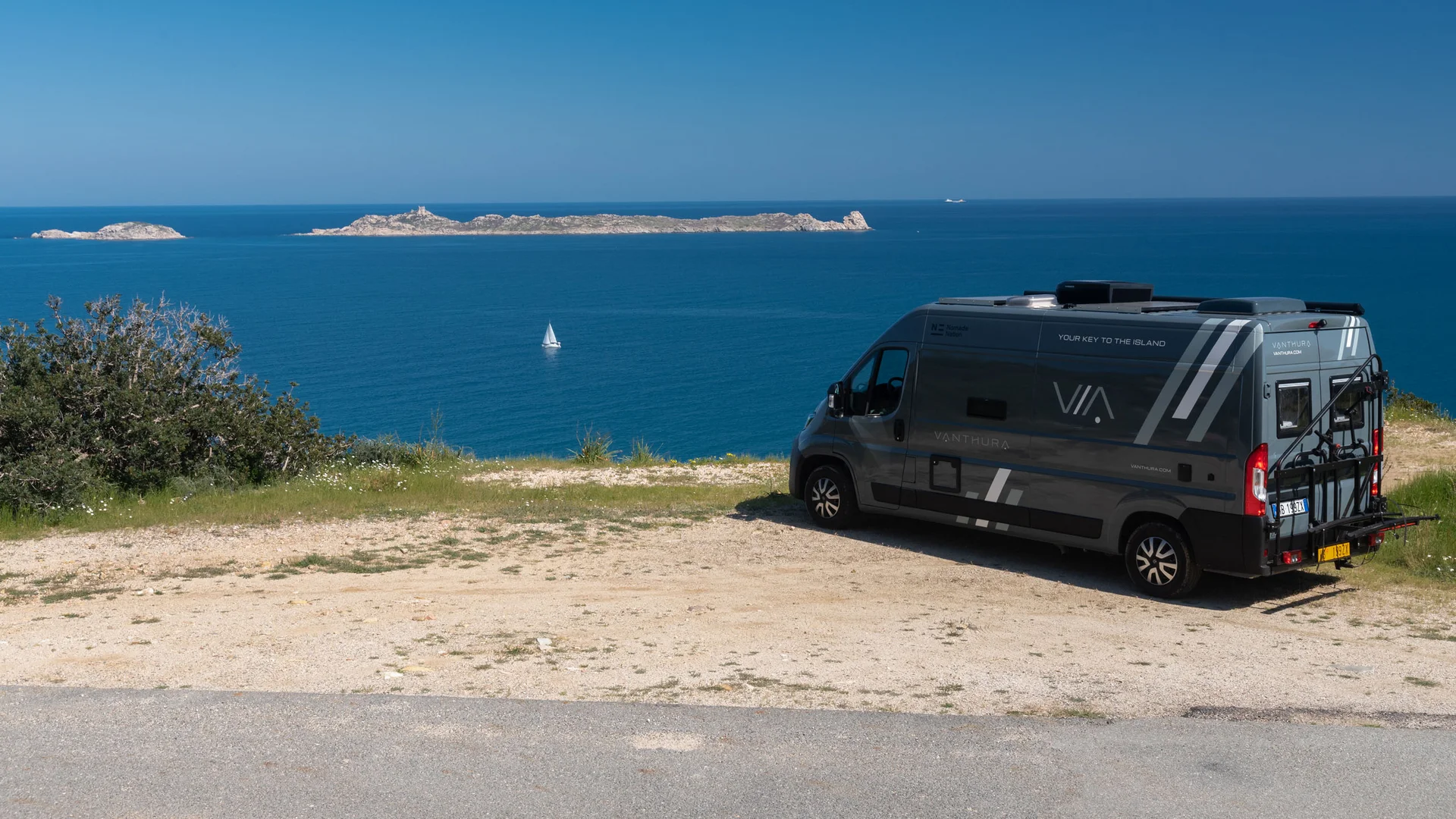 I nostri van sono targati Nomade Nation Camper parcheggiato vicino al mare con isole e una barca a vela sullo sfondo