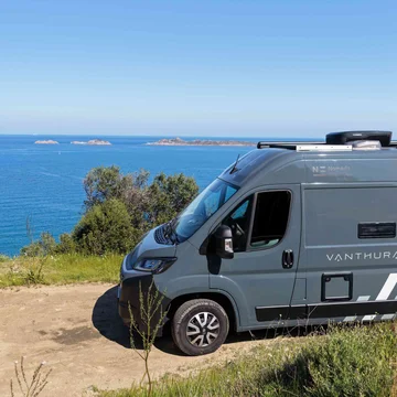 Camper grigio parcheggiato su strada sterrata vicino al mare con isole sullo sfondo