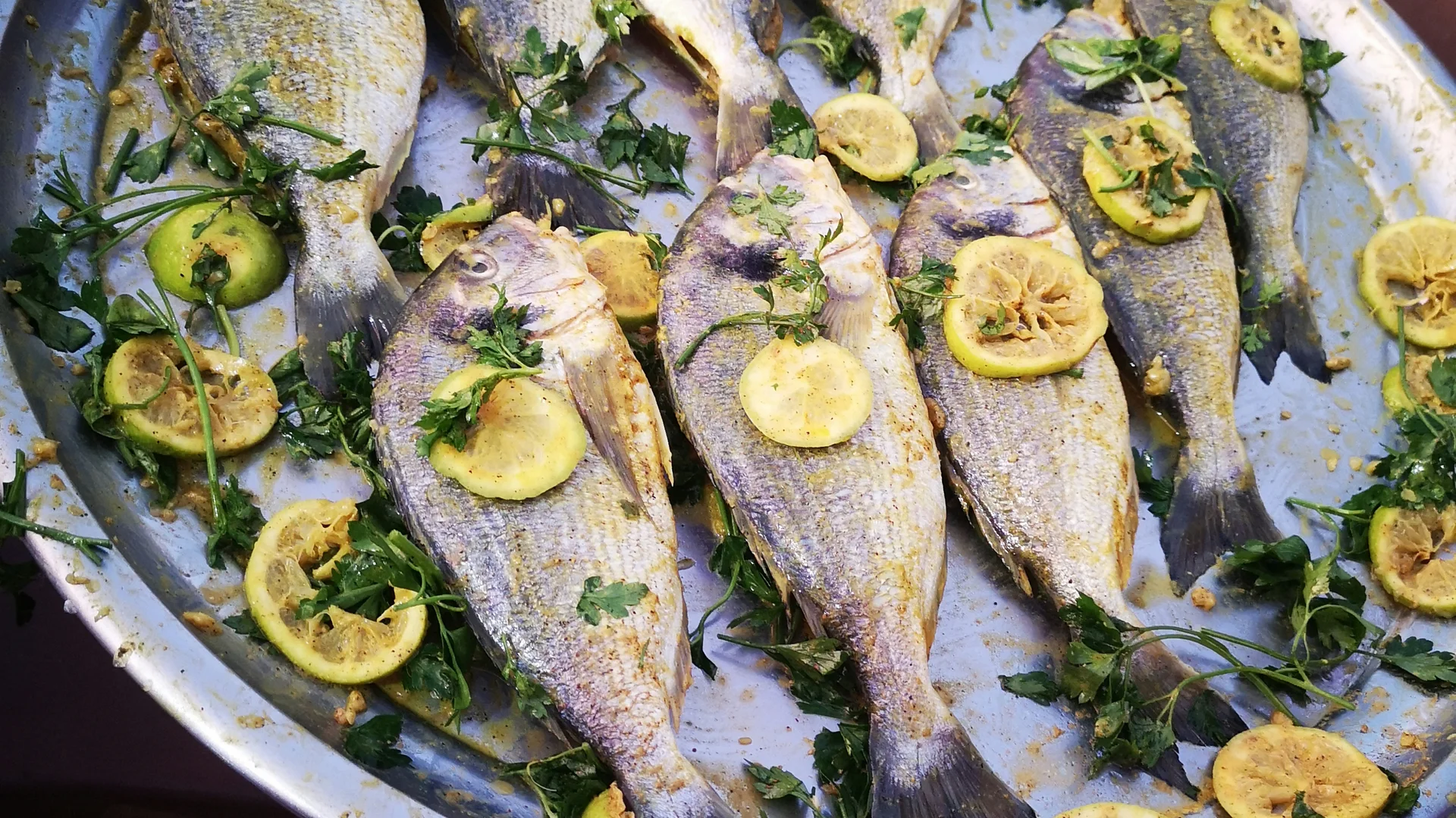 Pesci conditi con limone e erbe su un vassoio metallico