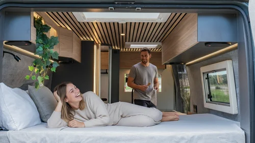 Coppia sorridente nel letto di un camper moderno e accogliente.