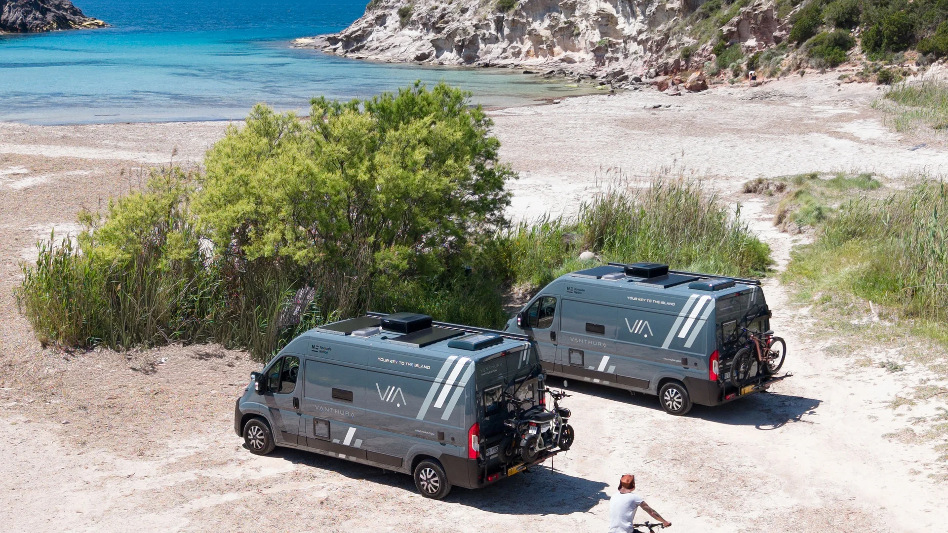Zwei Wohnmobile am Strand mit Radfahrer im Vordergrund am Meer
