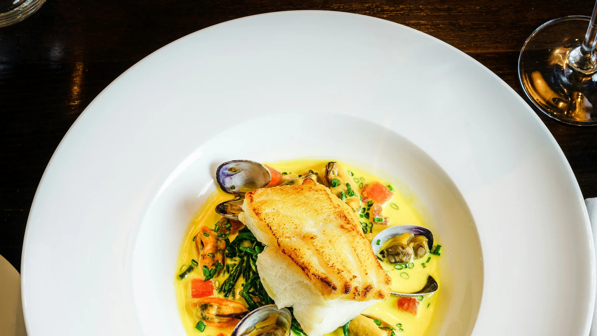 Piato elegante con pesce, vongole e salsa cremosa su tavolo scuro