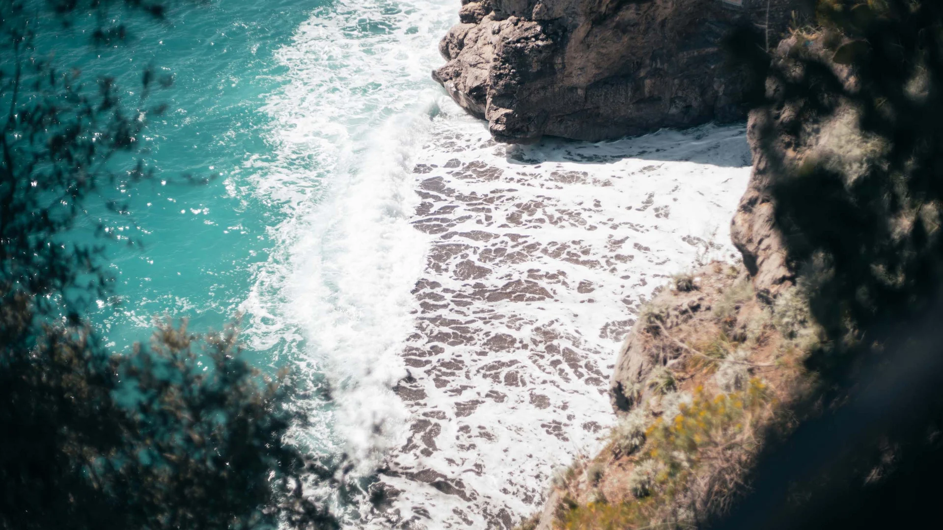 Vista dall'alto sulla costa rocciosa con onde bianche e mare turchese