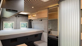 Interno moderno di un camper con letto, specchio e seduta chiara