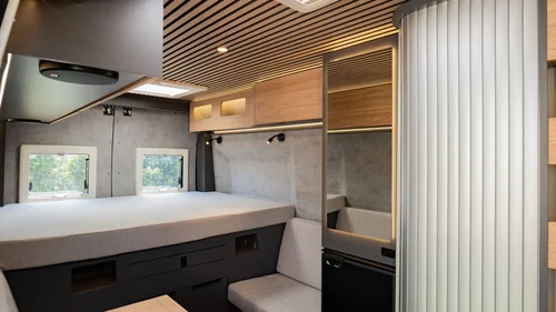 Interno moderno di un camper con letto, specchio e seduta chiara