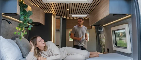 Coppia sorridente nel letto di un camper moderno e accogliente.