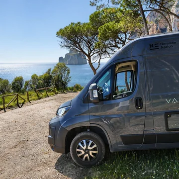 Furgone scuro parcheggiato su strada sterrata vista mare con alberi e scogliere