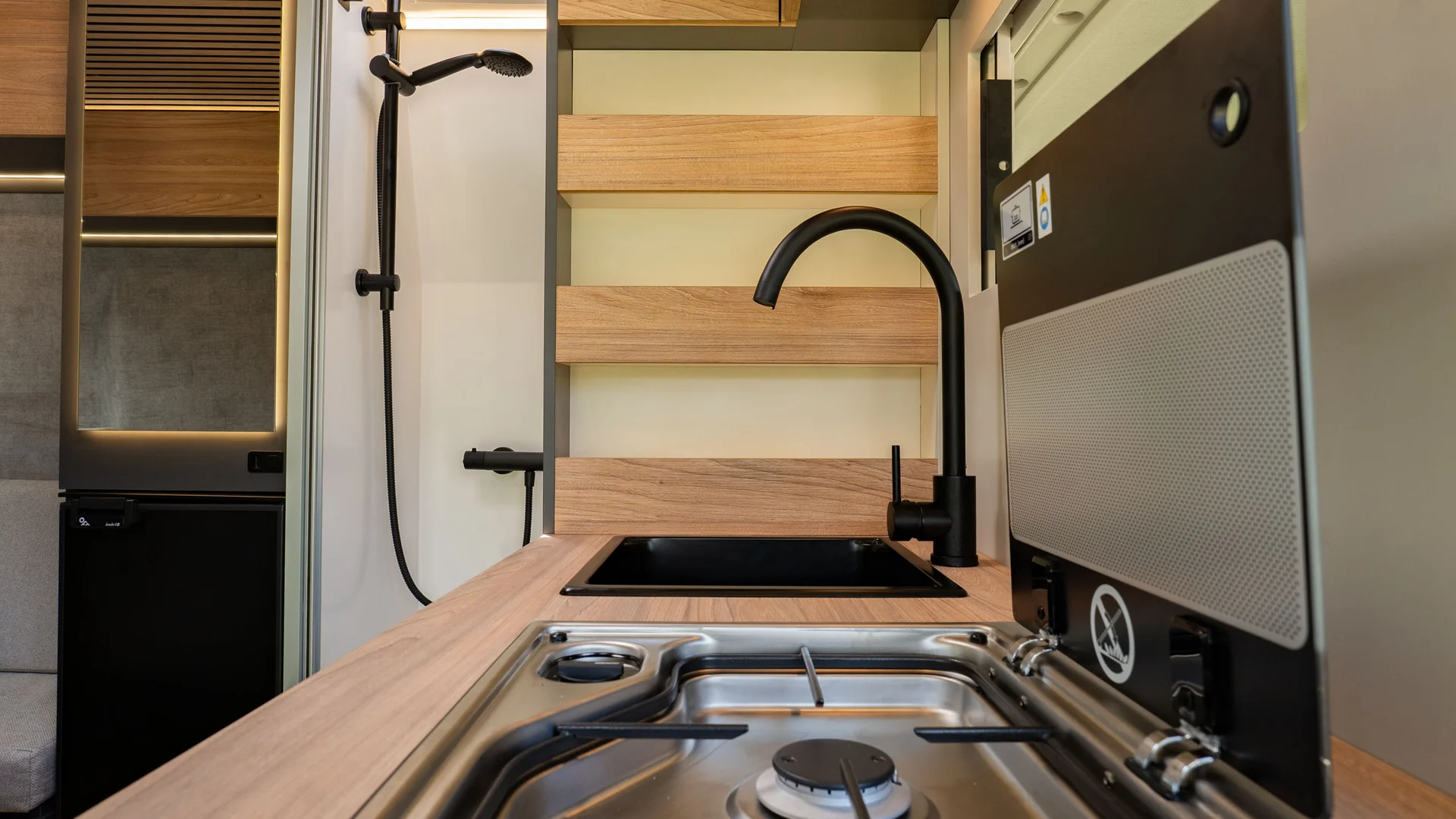 Cucina compatta in camper con fornello a gas, lavandino e doccia