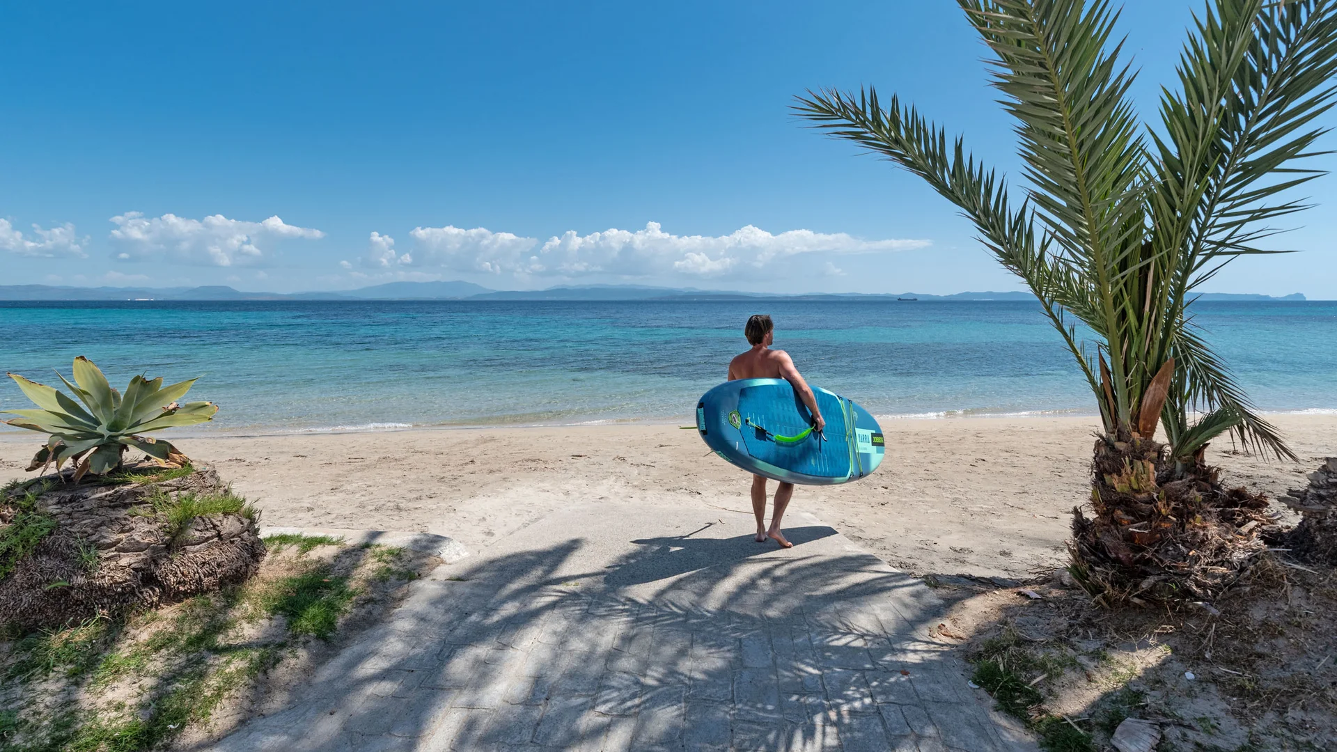 Mann mit Surfbrett schaut aufs Meer an einem tropischen Strand