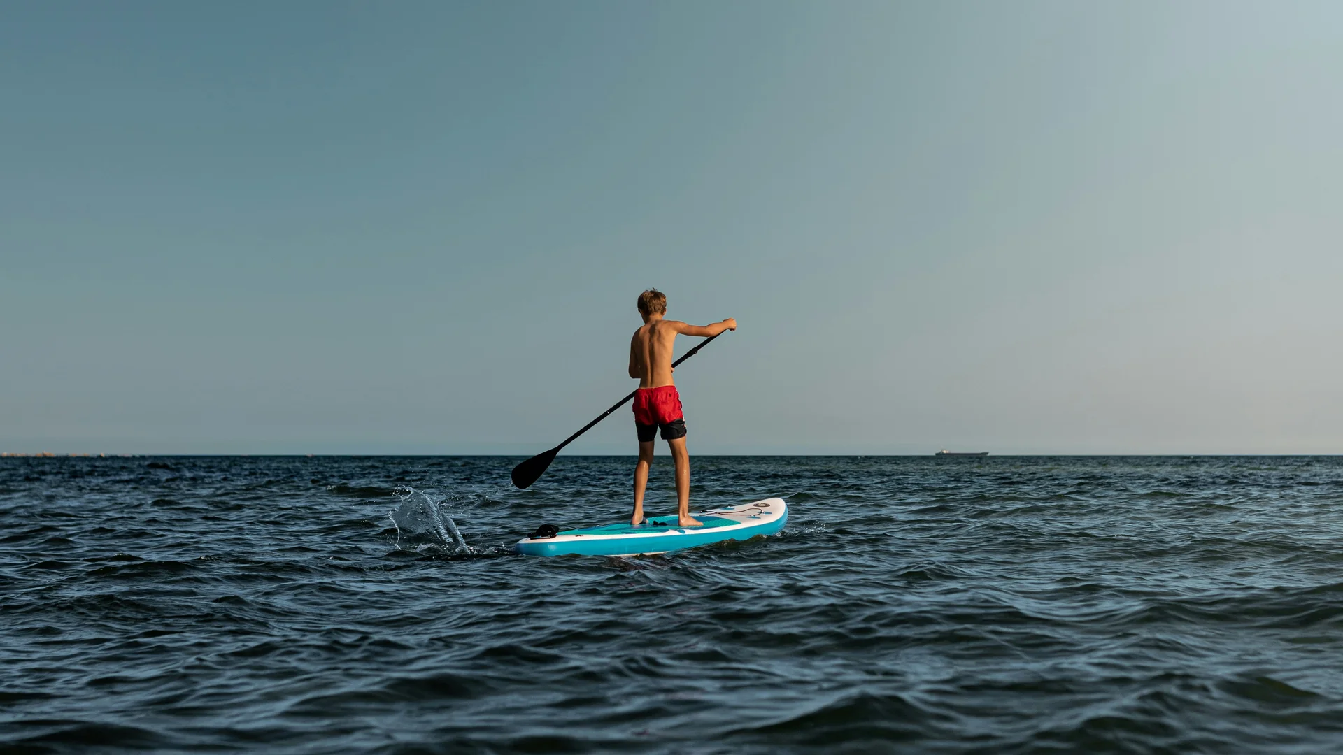 Ragazzo su tavola da paddle nella vasta distesa d'acqua sotto il cielo chiaro