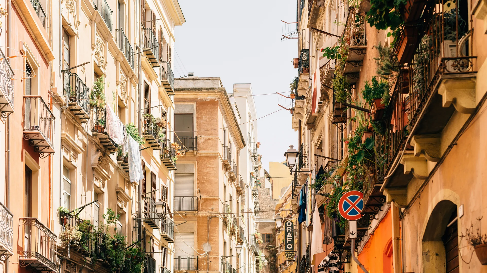 Stretta via tra edifici con balconi pieni di piante e panni stesi